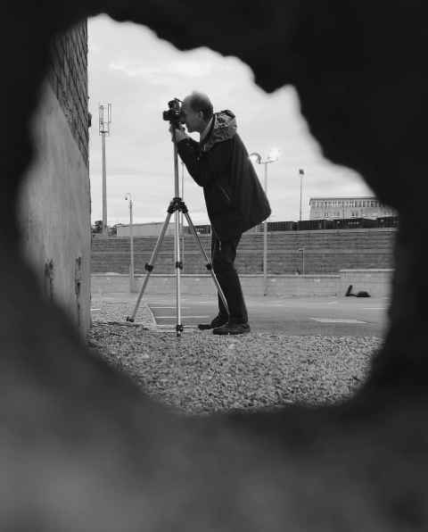 a picture taken through a hole in a concrete block of the photographer taking a picture with camera on tripod